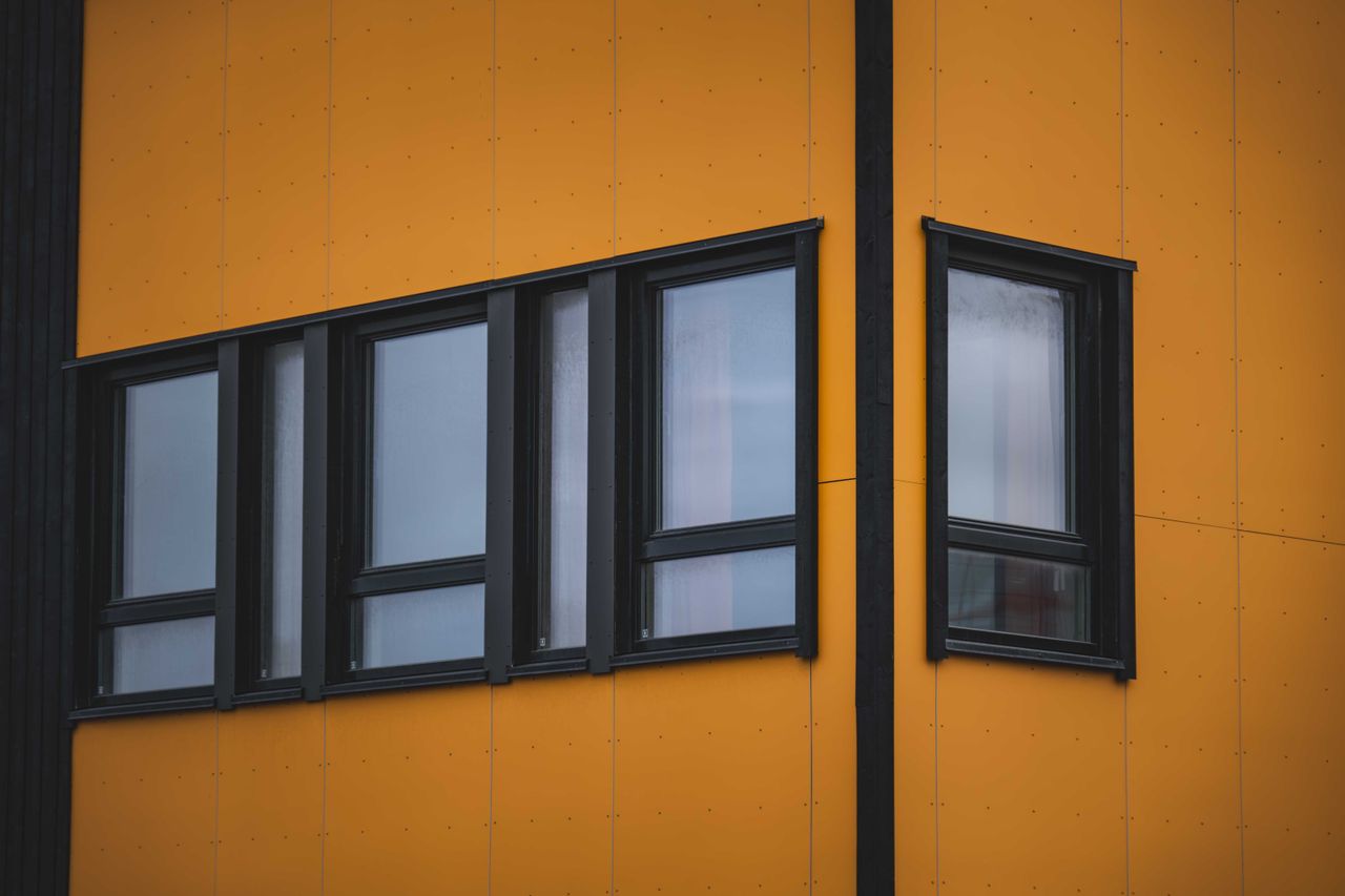 our-mission Architectural detail of a modern building facade with a vibrant yellow exterior and multiple windows.