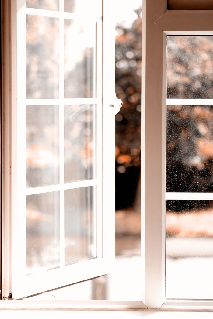 Bright image of an open white window frame with a view of autumn foliage, light and airy mood.