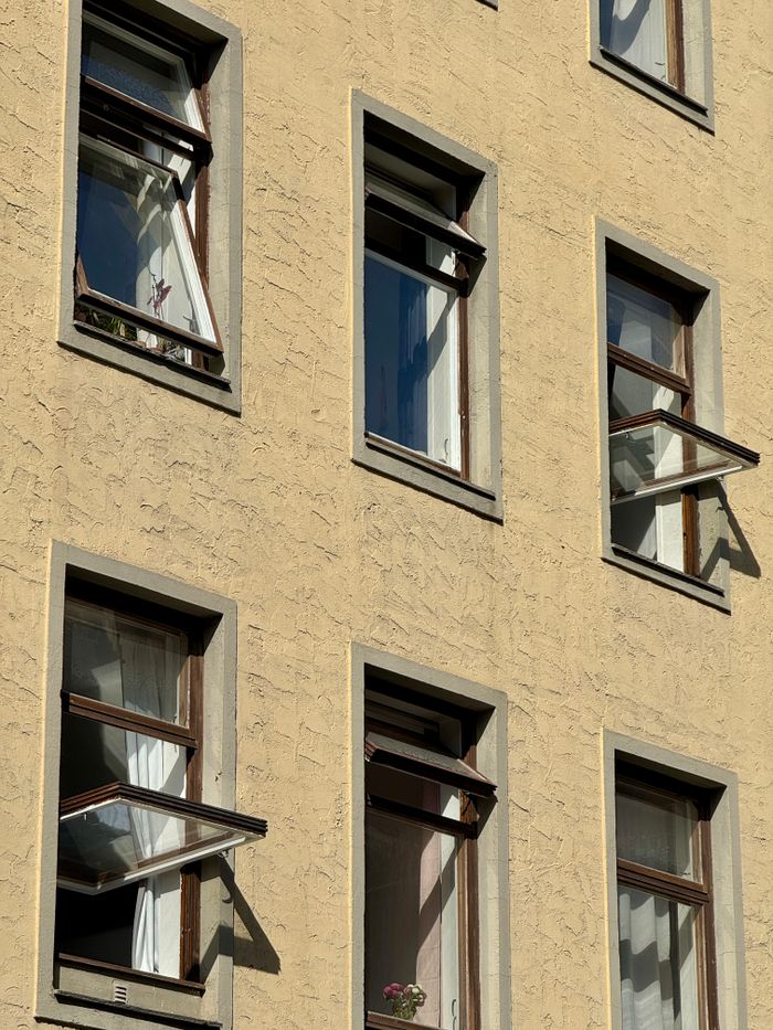 Facade of an apartment building in Oslo with open windows and sunlight casting shadows.