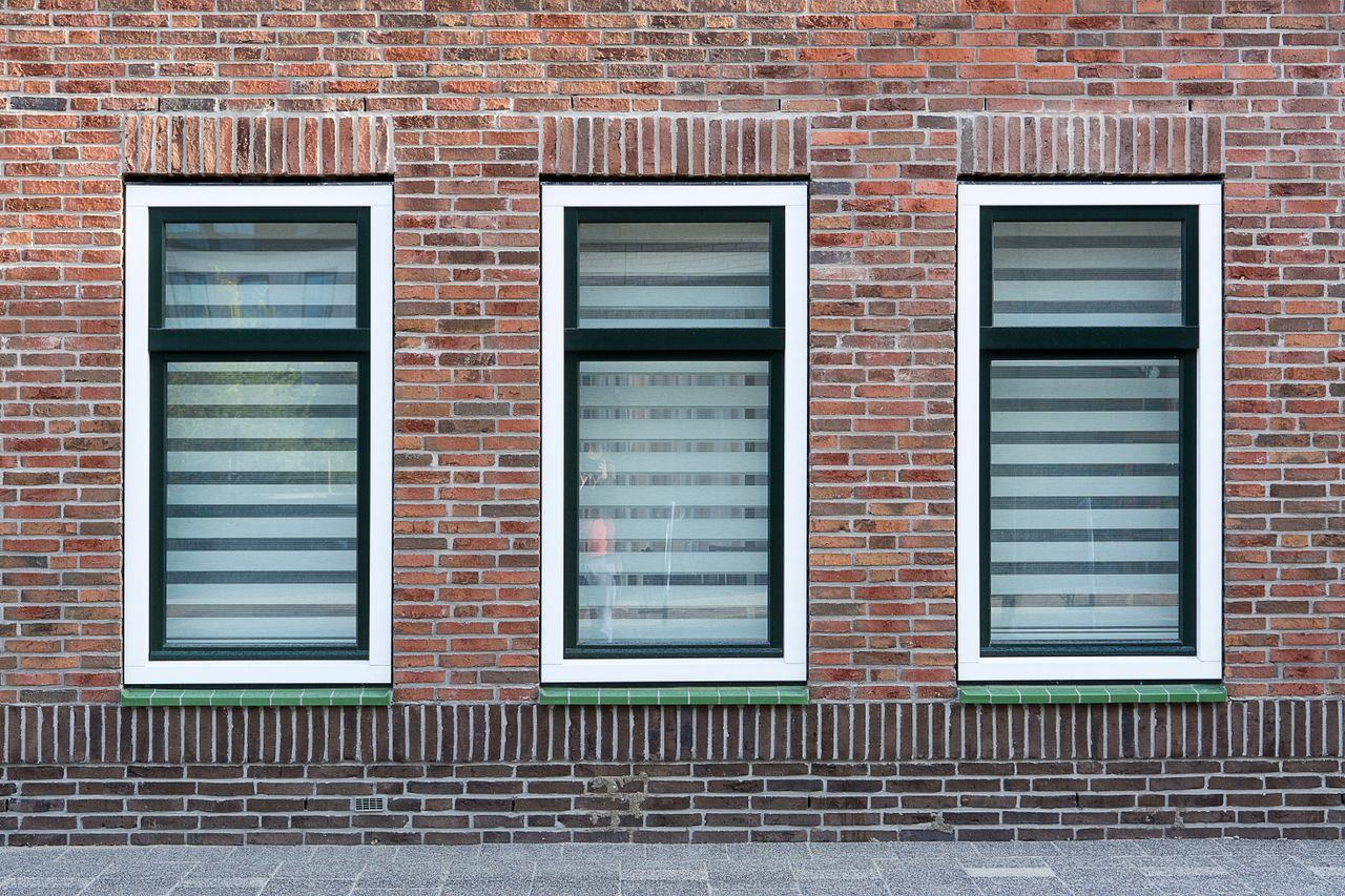 creative-approach-img A modern brick wall with three symmetrical windows featuring black and white striped blinds.